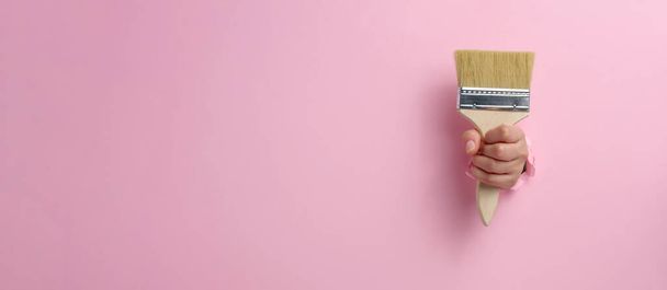 γυναικείο χέρι κρατήσει νέο πινέλο χρώμα με ξύλινη λαβή σε ροζ φόντο, αντίγραφο χώρου. Μπάνερ - Φωτογραφία, εικόνα