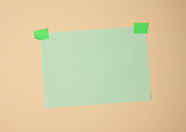 folha verde em branco retangular colada com papel pegajoso verde sobre fundo marrom claro, espaço de cópia - Foto, Imagem