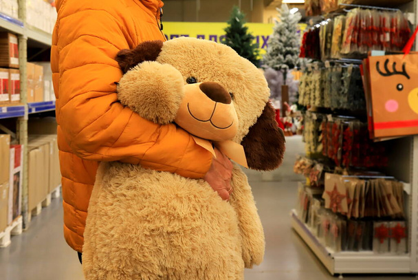 Een man kocht een grote teddybeer in de winkel, een cadeau voor een kind voor zijn verjaardag, Kerstmis, nieuwjaar. Kerstinkopen in winkelcentrum, winkel, supermarkt 2022 - Foto, afbeelding