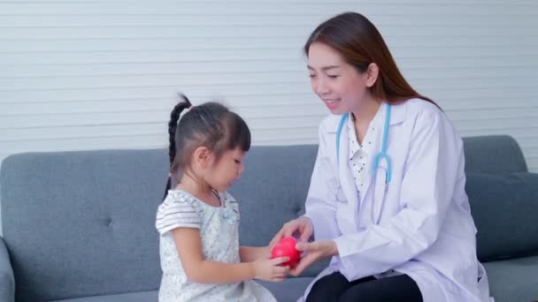 Ázsiai gyönyörű nő orvos egészségügyi ellenőrzés aranyos kislány Mindketten ült a kanapén. A kórházakban nyújtott orvosi szolgáltatások fogalma, gyermekegészségügyi ellenőrzések. - Felvétel, videó