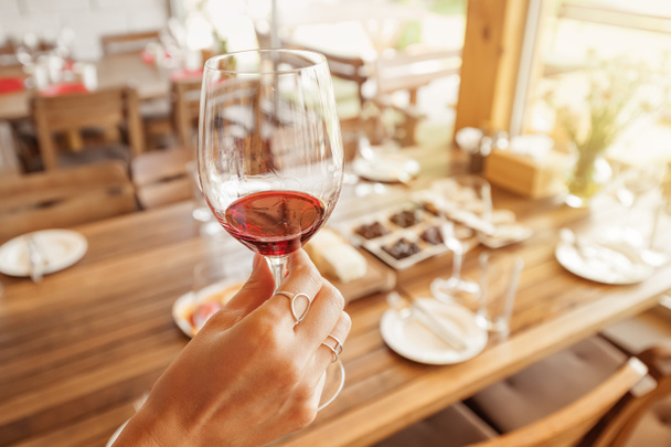 γυναικείο χέρι με νόστιμο κόκκινο κρασί σε οινοποιείο κατά τη διάρκεια ειδικής ξενάγησης. Η έννοια της ανθοδέσμες και νέες γεύσεις από τις καλύτερες ποικιλίες σταφυλιών και επιτραπέζιων ποικιλιών. - Φωτογραφία, εικόνα