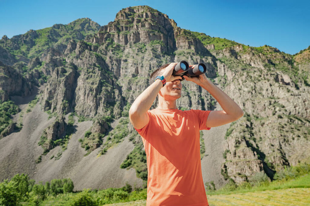 Un hombre con prismáticos está buscando aves o animales en una zona montañosa. Observación de aves y concepto de biólogo - Foto, Imagen
