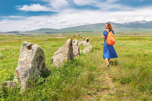 Счастливая женщина-путешественница с рюкзаком прогуливается по археологическим раскопкам Карауня и Зораца Карера в Армении. Туристические и таинственные места - Фото, изображение