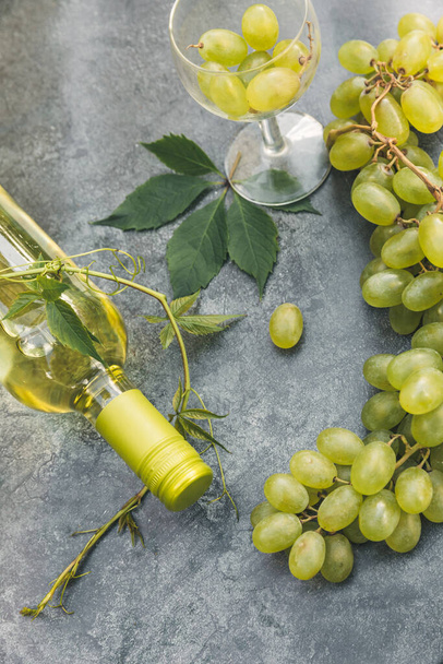 Top kilátás palack fehér bor, zöld szőlő, borosüveg és érett szőlő vintage szürke kő asztal háttér. Borbolt borozó borászat vagy borkóstoló koncepció. - Fotó, kép