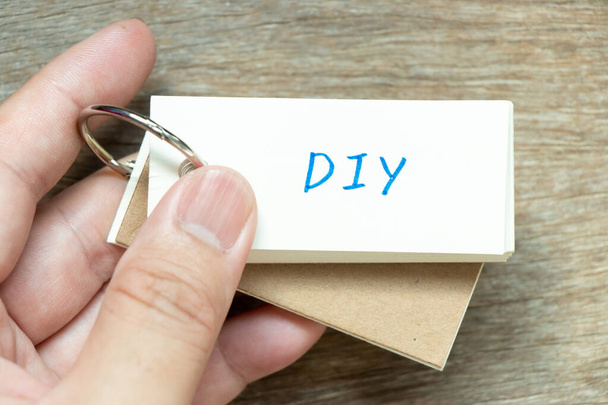 Man hold the flash card with handwriting word DIY (abbreviation of do it yourself) on wood background - Photo, Image