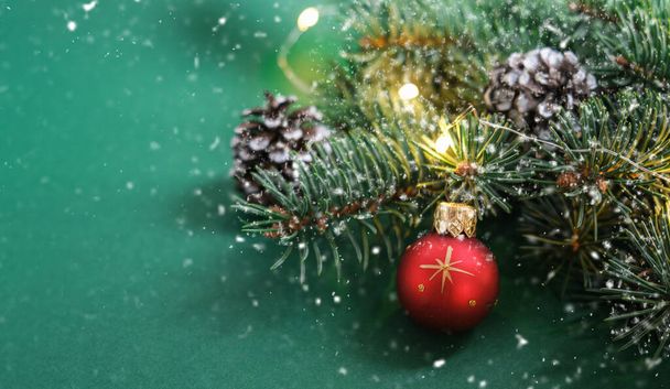 Christmas red ball, Christmas tree, cones and defocused lights on green background. Snow.Concept: Christmas and New Year, winter holiday theme. Selective focus. Copy space for text - 写真・画像