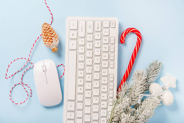 Escritório em casa de Natal com teclado, ramos de pinho e itens de Natal em um fundo azul. Layout plano, vista superior, espaço de cópia - Foto, Imagem