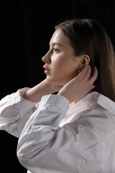 Profile of a beautiful girl in a white shirt on a dark background. - Photo, Image