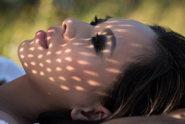 Portré fiatal nő feküdt a füvön napsugarakkal az arcán - Fotó, kép