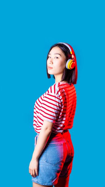 Молода азіатська жінка позує в бездротових навушниках Bluetooth, слухаючи музику, що транслюється, дивлячись камеру ізольовану рекламну копію
 - Фото, зображення