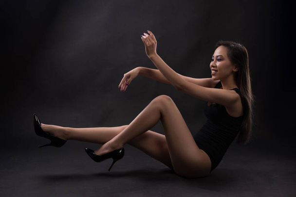 Young slim asian woman in black bodysuit posing at studio - Фото, изображение
