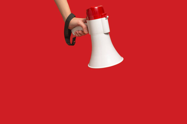 Megafoon in vrouwenhanden op een rode achtergrond. Kopieerruimte.  - Foto, afbeelding