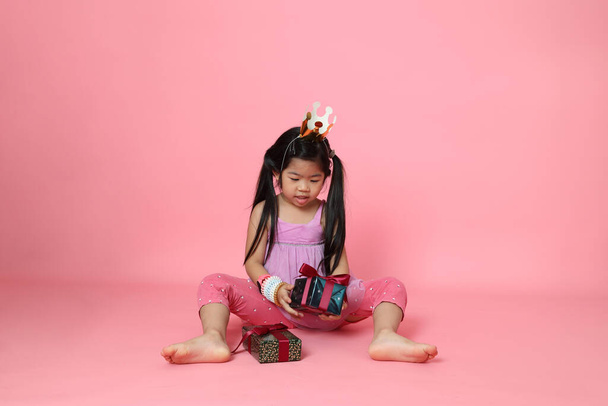 A fiatal ázsiai lány ül jelen dobozok a rózsaszín háttér. - Fotó, kép
