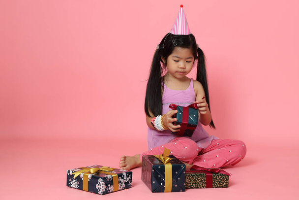 La joven asiática sentada con cajas de regalo sobre el fondo rosa. - Foto, imagen