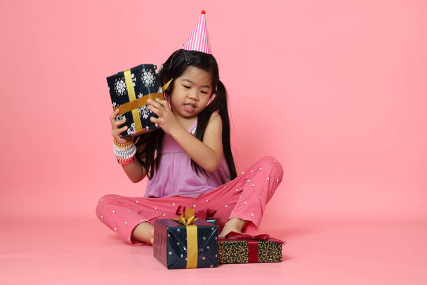 A fiatal ázsiai lány ül jelen dobozok a rózsaszín háttér. - Fotó, kép