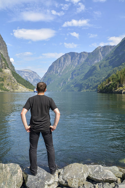 Vista posterior del hombre mirando y disfrutando de la vista sobre el lago y los fiordos en el día claro de verano cerca de Naeroyfjord en el pueblo de Gudvangen, Noruega - Foto, imagen