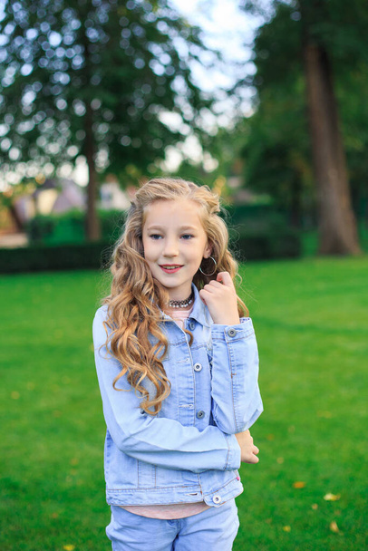 Menina de cabelos loiros, de olhos azuis em um terno azul contra um fundo parque verde. Um retrato alegre de uma menina em um espaço aberto. - Foto, Imagem