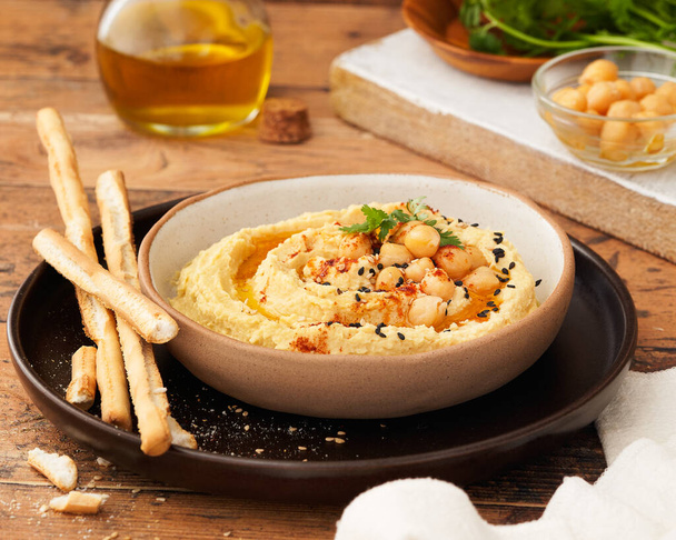 Homemade hummus with bread sticks and parsley on wooden background copy space. Selective focus. Middle Eastern vegan pate side dish, delicious appetizer, snack, or spread. Vegetarian food concept. - Fotografie, Obrázek