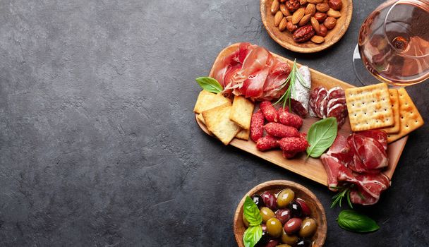 Antipasto board με προσούτο, σαλάμι, κράκερ, τυρί, ξηρούς καρπούς, ελιές και ροζέ κρασί. Πάνω όψη επίπεδη θέσει με αντίγραφο χώρου - Φωτογραφία, εικόνα