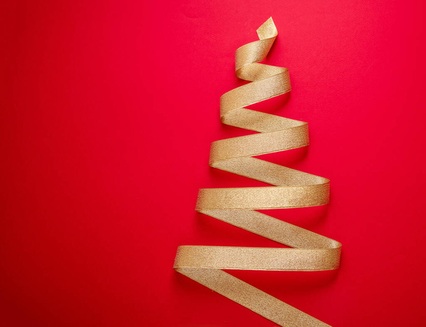 Veselé Vánoce a šťastný Nový rok přání šablony. Vánoční strom tvar zlatá stuha na červeném pozadí barvy. Zlatá lesklá kudrnatá páska, minimální provedení.  - Fotografie, Obrázek