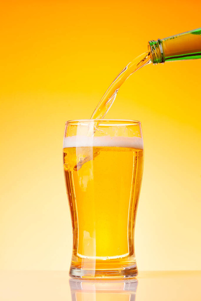Beer pouring from bottle into glass in front of yellow background. Studio shot - 写真・画像