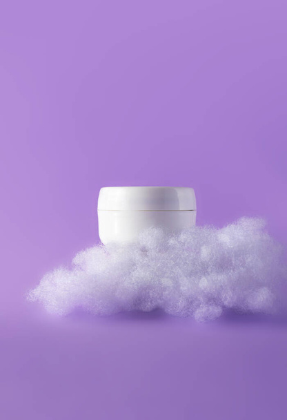 Blank cosmetic skin care makeup jar with fluffy clouds on violet. Concept care with sensitive skin. Creative still-life photo, vertical - Photo, Image