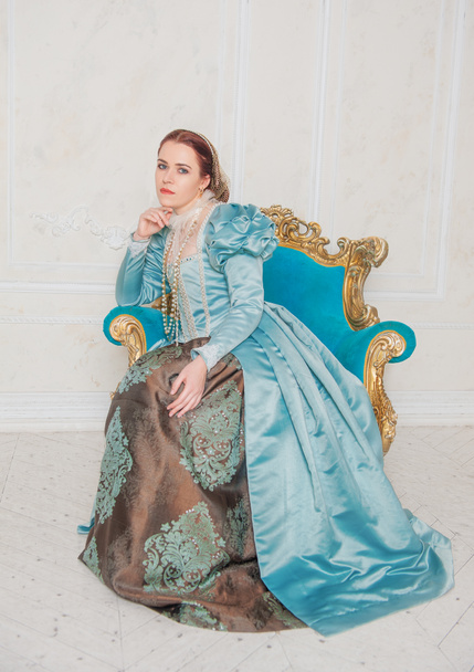 Beautiful young woman in medieval style blue dress sitting in the armchair - Photo, Image