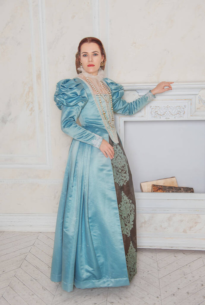 Belle jeune femme dans le style médiéval robe bleue dans la chambre près de la cheminée - Photo, image