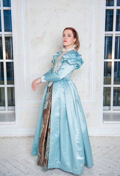Hermosa mujer joven de estilo medieval vestido azul de pie en la habitación - Foto, imagen