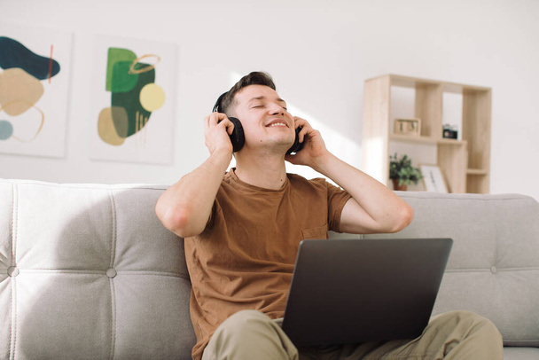 jonge man ontspannen op de sofa met koptelefoon in de woonkamer - Foto, afbeelding