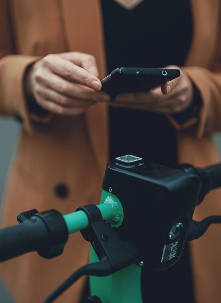 Жінка використовує додаток на смартфон, щоб розблокувати електричний скутер на вулиці
. - Фото, зображення