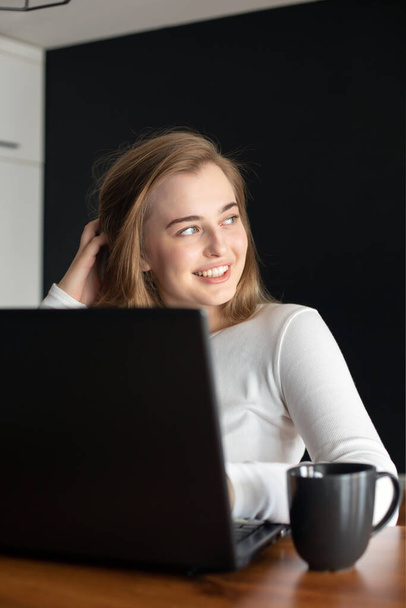 Jonge vrouw lacht en kletst online op een laptop thuis of op kantoor. Concept van online studeren of thuiswerken.Rust tijdens het werk. - Foto, afbeelding