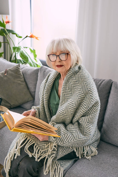 vieille femme âgée assise sur le canapé lisant un livre à la maison. Éducation, mature, concept de loisirs - Photo, image