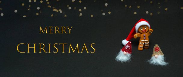 Christmas concept. Gnomes and gingerbread man in santa hat on black background with text, close up. Banner - Photo, Image