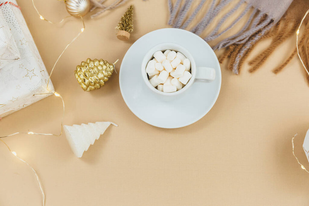 Cup of coffee, gift box and knitted scarf, led lights on beige background. Hygge style, winter concept. Cozy home desk. New year and Christmas celebration mockup. Christmas still life - Zdjęcie, obraz