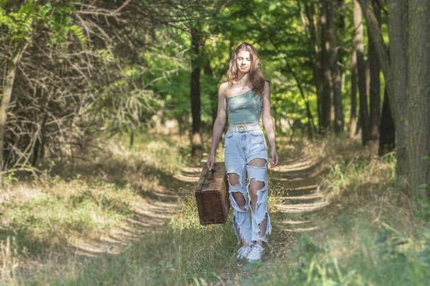 Młoda kobieta spacerująca po leśnej drodze z brązową walizką - Zdjęcie, obraz