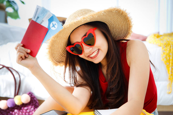 Young happy and excite Asian female traveler getting ready for a summer holiday trip vacation with her bright yellow suitcase wearing heart shape sunglasses holding passport plane ticket. - Foto, immagini