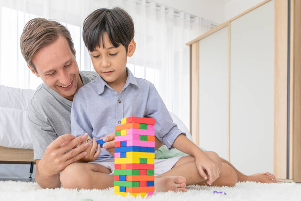 Father and his mixed-race son playing colorful wooden block together with joy and happiness in home bed room. Idea for learning and sharing good time. - Foto, afbeelding
