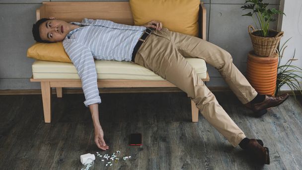 Hombre asiático borroso acostado en el sofá con un montón de diferentes drogas y pastillas después de intentar el suicidio conmutado. Concepto de problema de vida. - Foto, imagen