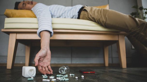 Rozmazaný asijský muž ležící na pohovce s množstvím různých léků a pilulek po pokusu dojíždět sebevraždu. Life problem concept. - Fotografie, Obrázek