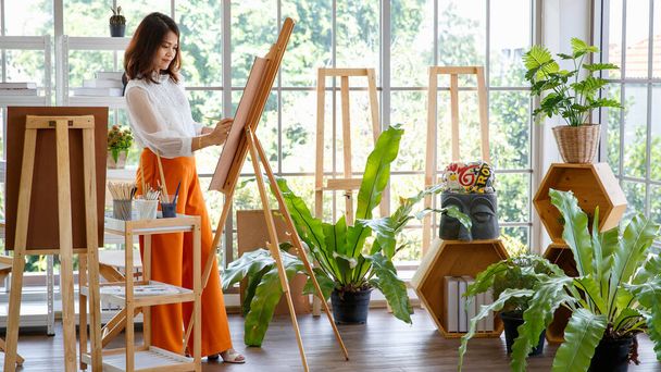 Seniorin Malerin Bild im Atelier zu Hause mit grünem Bäumchen in kleinem Garten und voller natürlichem Licht. - Foto, Bild
