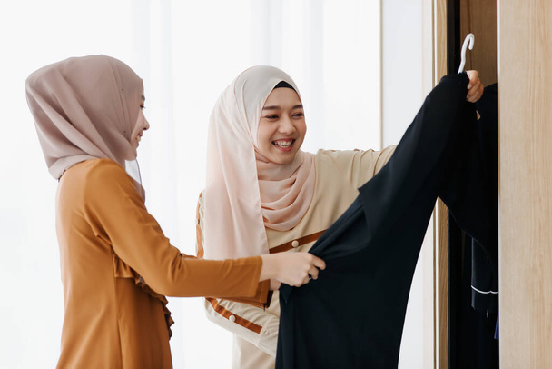 Dwie azjatyckie muzułmanki wybierające ubrania razem ze szczęściem. - Zdjęcie, obraz
