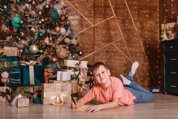 a nine-year-old boy lies on his stomach and writes on the foliage of the paper his wishes for Christmas - Photo, Image