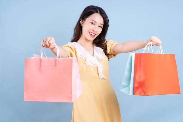 Beautiful young Asian woman holding shopping bag on blue background - Fotografie, Obrázek