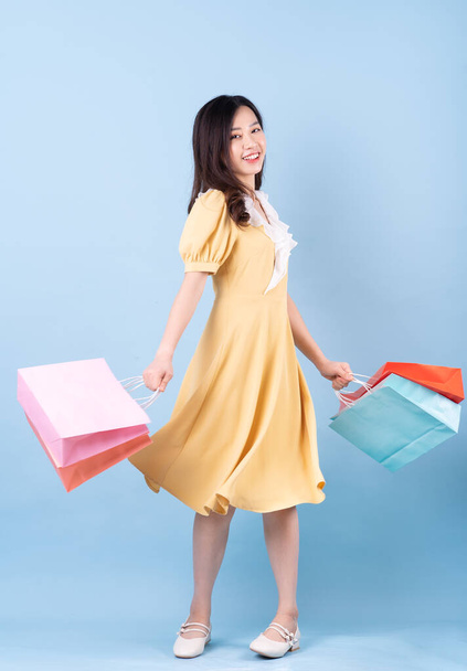Beautiful young Asian woman holding shopping bag on blue background - Фото, изображение