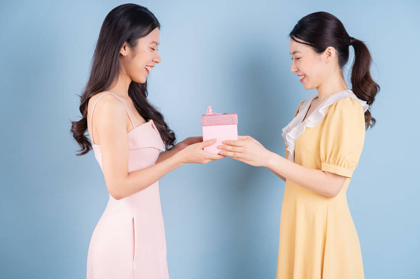Twee jonge Aziatische vrouwen dragen jurk op blauwe achtergrond - Foto, afbeelding