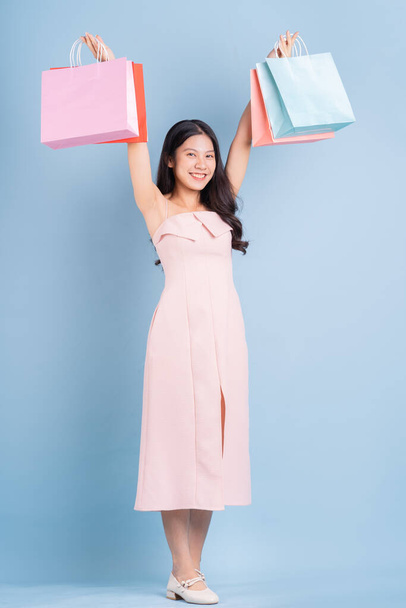 Beautiful young Asian woman holding shopping bag on blue background - Foto, Imagem