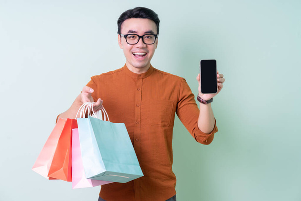 Young Asian man holding shopping bag on green background - Foto, afbeelding