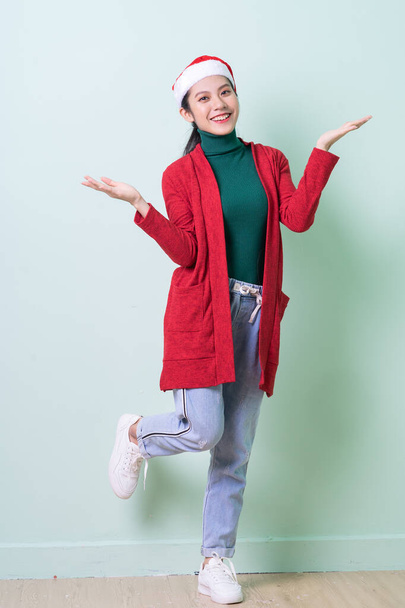 Mujer asiática joven con sombrero de Navidad sobre fondo verde, concepto de x-mas - Foto, imagen