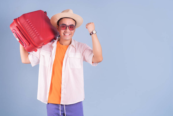Fiatal ázsiai férfi kezében piros bőrönd kék háttér - Fotó, kép